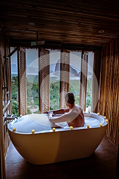 Men watching sunset in bathtub in the bathroom during vacation in Thailand watching sunset over the ocean and moutnains photo