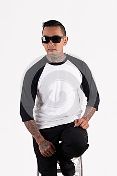 A men wearing blank plain t shirt  on white background. Hipster man wearing raglan 3/4 sleeve and sunglasses sitting in a