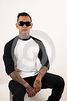 A men wearing blank plain t shirt  on white background. Hipster man wearing raglan 3/4 sleeve and sunglasses sitting in a