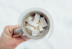 Men in winter forest hold mug with hot chocolate and marshmallow. Shot from above. Selective focus