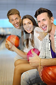 Men and woman hold balls, thumb up in bowling club