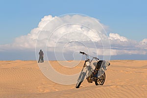 Men and woman with motorcycle in the desert against a cloudy sky background