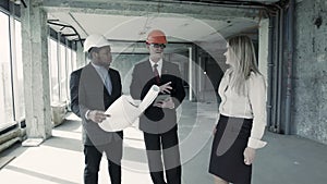 Men, woman in suit and helmet discuss blueprint, communicate with buyer. Chief engineer builder