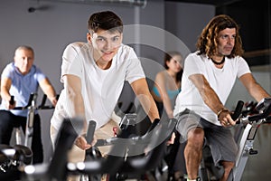 Man and woman taking indoor cycling class at fitness center, doing cardio riding bike