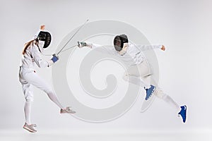 The men and woman wearing fencing suit practicing with sword against gray