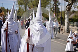 men women and children in a procession, with long white dresses and hoods