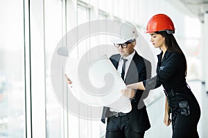 The man and woman in a helmets hold the project plan in the building. Construction business.