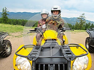 A man and woman of retirement age in camouflage suits and helmets ride a yellow ATV in the mountains. Sports, recreation