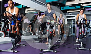 Men and women ride stationary bike in fitness club