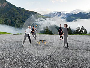 Men and women in their twenties playing a game of spike ball in a mountain parking lot in the Dolomites