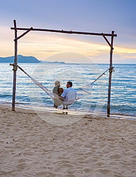 Men and women watching sunset from a hammock on the beach in Pattaya Thailand Ban Amphur beach