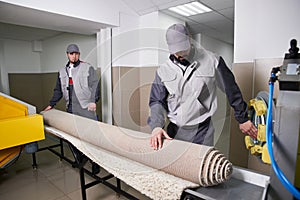 Men workers get carpet from an automatic washing machine and put in in dryer in the Laundry service