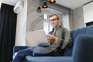 Men working on laptop computer in his room. Home work or study, freelance concept. Young man sitting relaxed on sofa
