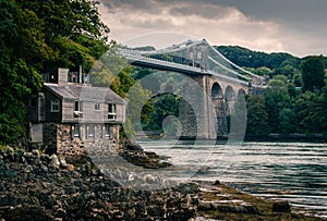 Menai suspension bridge in North Wales with boathouse in foreground on a gloomy day