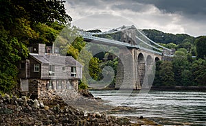 Menai suspension bridge in North Wales with boathouse in foreground on a gloomy day