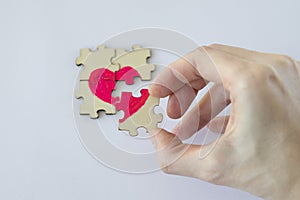 Mending Broken Heart. Woman& x27;s hand assembles a small puzzle from a wooden puzzle with a painted pink heart.