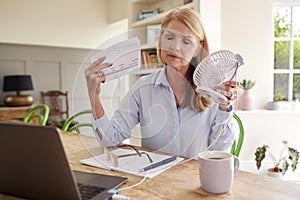 Menopausal Mature Woman Having Hot Flush At Home Cooling Herself With Fan Connected To Laptop