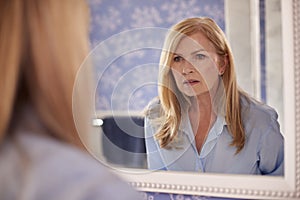 Menopausal Mature Woman Looking At Skin In Mirror At Home