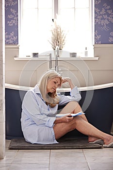 Menopausal Mature Woman Suffering With Incontinence Holding Pad Sitting On Toilet At Home