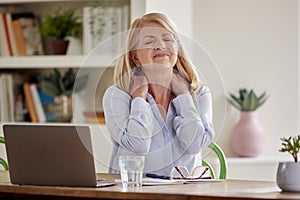Menopausal Mature Woman Suffering Neck Pain Working On Laptop At Home