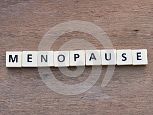MENOPAUSE crossword by square letter tiles against wooden background.