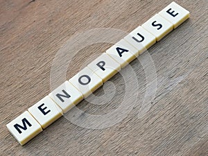 MENOPAUSE crossword by square letter tiles against wooden background.