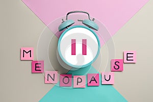 Menopause word of sticky notes with letters and alarm clock with pause symbol on color background, top view