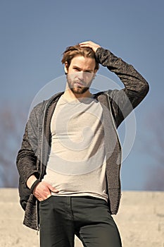 Mens fashion and style. Man with beard in casual wear touch hair on sunny outdoor, fashion. Macho stand on blue sky