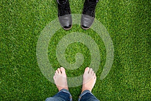 Mens feet resting on green grass standing opposite boots