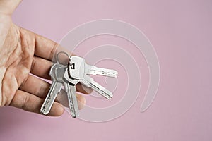 Mens hand holding a set of keys with a pink background. Realtor with a keys to an apartment for a clients. Focus on the