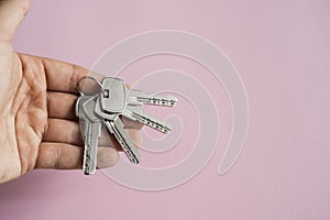 Mens hand holding a set of keys with a pink background. Realtor with a keys to an apartment for a clients. Focus on the