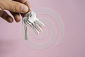 Mens hand holding a set of keys with a pink background. Realtor with a keys to an apartment for a clients. Focus on the