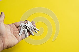 Mens hand holding a set of keys with a yellow background. Realtor with a keys to an apartment for a clients. Focus on