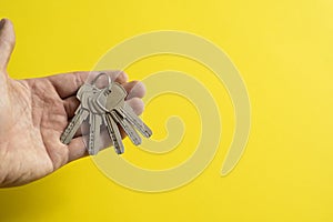 Mens hand holding a set of keys with a yellow background. Realtor with a keys to an apartment for a clients. Focus on