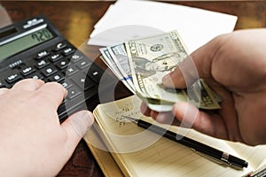 Mens hands is holding dollars and counting expenses on the calculator