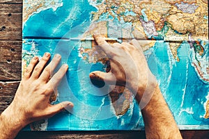 Mens Hands On A Paper Map Of The World Indicate The Final Destination, Top View photo