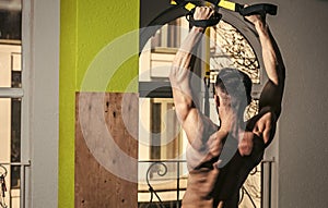 Mens heals body care. Sportsman, athlete, muscular macho does exercise with trx loops, window on background. Sport and