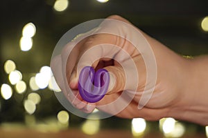 Menstrual Cup on red or black background in the girl hand, low key. woman hands folding a menstrual cup. lights in the background.