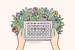 Menstrual cycle calendar in hands of woman and flowers, for tracking of PMS days photo