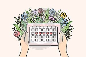 Menstrual cycle calendar in hands of woman and flowers, for tracking of PMS days