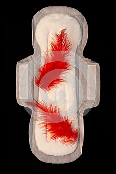 Menstrual pad with red feathers like blood drops on black background top view. Irregular period concept. Menorrhagia