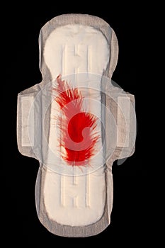 Menstrual pad with red feathers like blood drops on black background top view. Irregular period concept. Menorrhagia photo