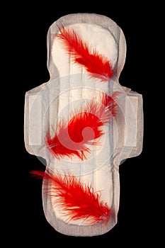 Menstrual pad with red feathers like blood drops on black background top view. Irregular period concept. Menorrhagia photo