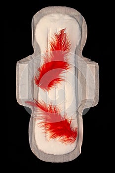 Menstrual pad with red feathers like blood drops on black background top view. Irregular period concept. Menorrhagia photo