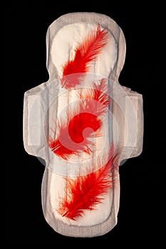 Menstrual pad with red feathers like blood drops on black background top view. Irregular period concept. Menorrhagia photo