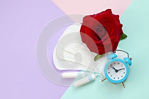 Menstrual pads and tampons with blue alarm clock and red rose flower on multicolored background