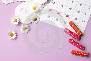 Menstrual pads and tampons on menstruation period calendar with chamomiles on pink background