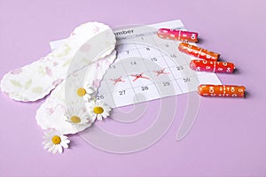 Menstrual pads and tampons on menstruation period calendar with chamomiles on pink background