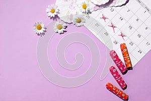 Menstrual pads and tampons on menstruation period calendar with chamomiles on pink background