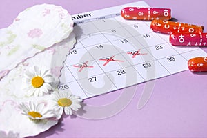 Menstrual pads and tampons on menstruation period calendar with chamomiles on pink background